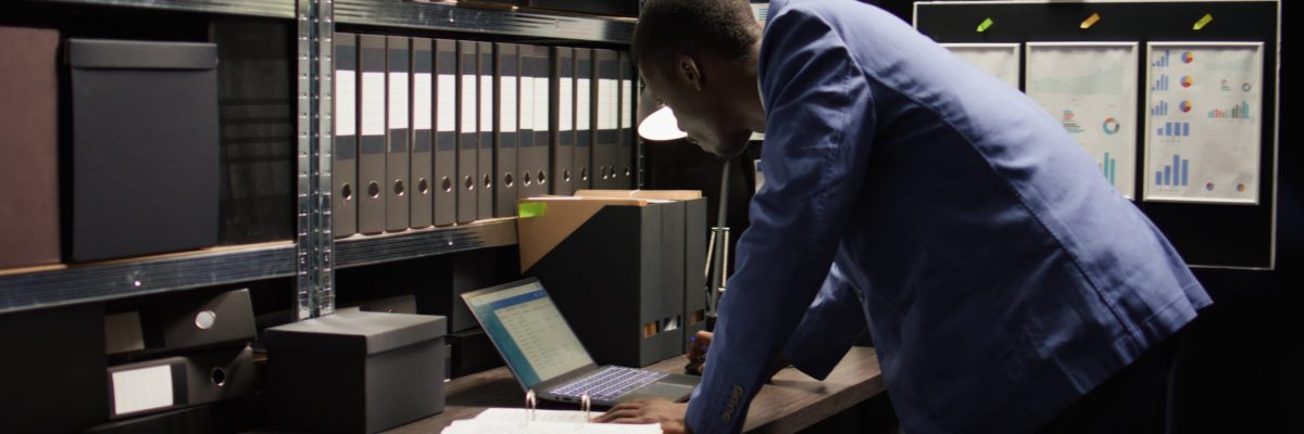 In neatly organised office, african american detective examines evidence with intention of solving crimes. Committed police officer walks up to his desk carrying case file for criminal investigation.